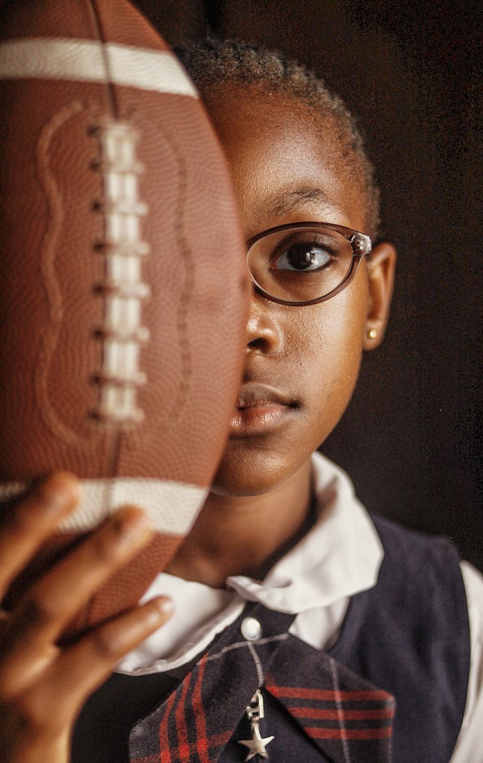 Portrait of a young girl in Nigeria holding an American football, showing determination and focus.